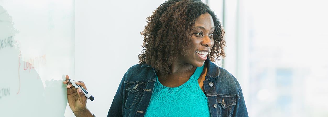 A woman at a whiteboard smiling.