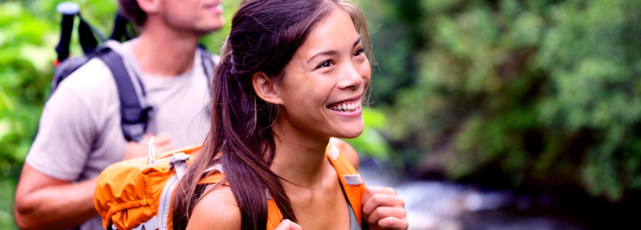 A woman and man, both smiling, hiking outdoors with backpacks.